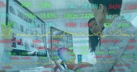 Viewing two in blazers leaning on laptop at office monitor showing colorwheel tickers, copy space