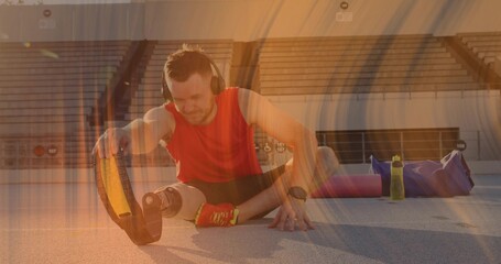 Stretching man with prosthetic blade wearing red top and black shorts on track, with headphones