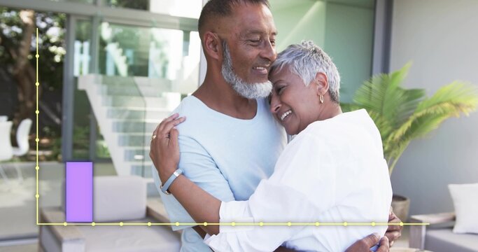Embracing senior couple leaning at home near glass doors wearing blue shirt white top with chart