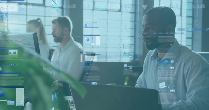 Working man in light blue button-up shirt typing on laptop at open-plan office, with data overlays