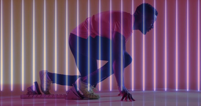 Crouching man planting hand, bracing foot on block in studio with neon lights, wearing pink shirt