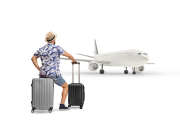 Rear view shot of a man sitting on a suitcase and looking at a plane