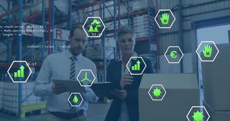 Reviewing pallets, two business managers holding tablet and clipboard in warehouse with green icons