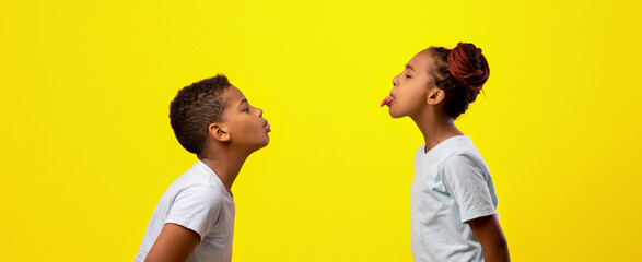 Two kids stand close together, making silly faces at one another. One child sticks out their tongue...