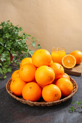Fresh Navel Oranges in Wicker Basket with Orange Juice and Green Herbs on Dark Slate Kitchen Counter