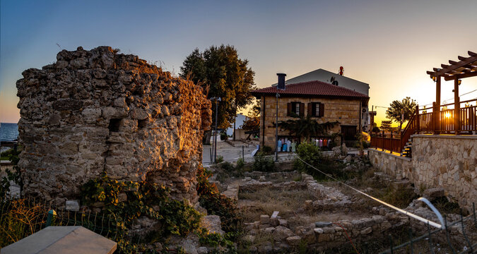 Ancient Roman stone wall with rusticated blocks illuminated by warm evening sun, traditional Mediterranean houses with tile roofs and sea horizon in historic old town. Side, Antalya, Turkey.

