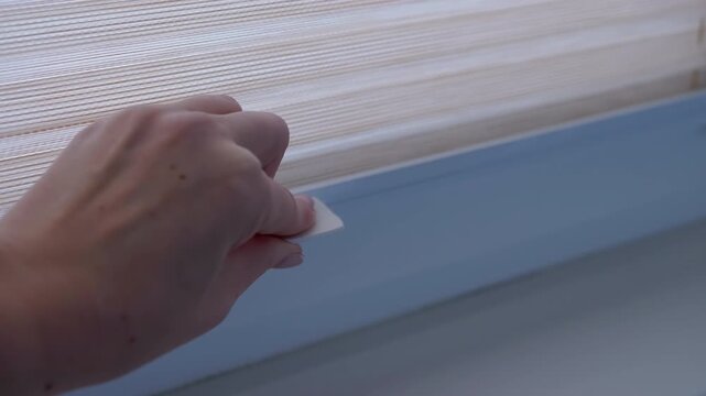 A hand raises pleated blinds, letting in natural light and revealing the view from a window. Perfect for home and interior projects.