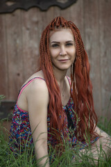 Young woman with vibrant braided hair, wearing a colorful floral dress, poses playfully outdoors, showcasing a cheerful expression and a sense of freedom in a natural setting