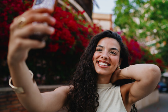 Happy woman adjusts hair while taking selfie, blending personal style with mobile-first digital identity in a connected lifestyle.