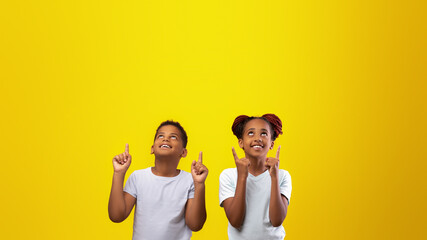 Two children stand smiling and pointing upwards, expressing excitement and happiness. The bright...