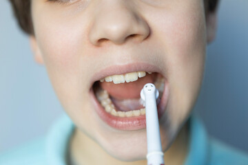 Child brushing teeth with electric toothbrush indoors during morning routine in bright, clean bathroom