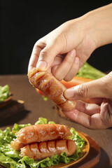 Grilled Bacon-Wrapped Sausage Being Held Over Wooden Plate with Fresh Lettuce for BBQ Cooking