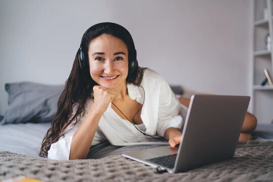 Confident young woman with headphones leans on hand and smiles at camera during online interaction, embodying personal branding and approachability in digital freelance lifestyle.