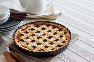 Freshly baked lattice pie on a rustic table beside stacked plates, bowls, and a white teapot, creating a cozy homemade dessert scene.