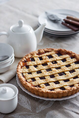Freshly baked lattice pie on a rustic table beside stacked plates, bowls, and a white teapot, creating a cozy homemade dessert scene.
