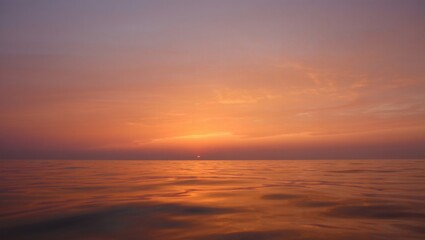 Obraz premium Golden hour sun setting over the calm horizon of a vast ocean, creating vibrant orange and purple reflections on the tranquil water surface and sky
