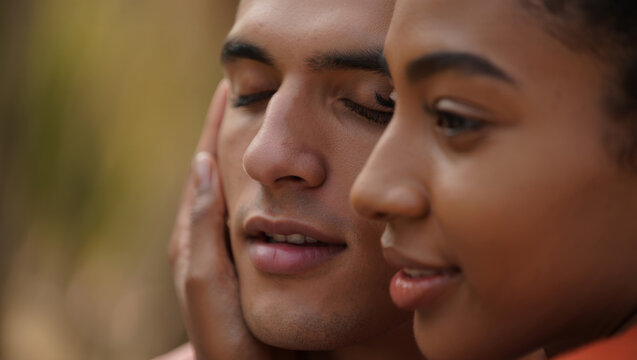 Affectionate diverse young couple sharing a tender moment, woman gently touching man's face with eyes closed, expressing intimacy, love, and connection outdoors