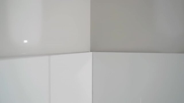 Sleek white rectangular tiles form a minimalist geometric wall pattern, glossy surfaces catching shifting light and shadow to create a subtle sense of motion and modern depth