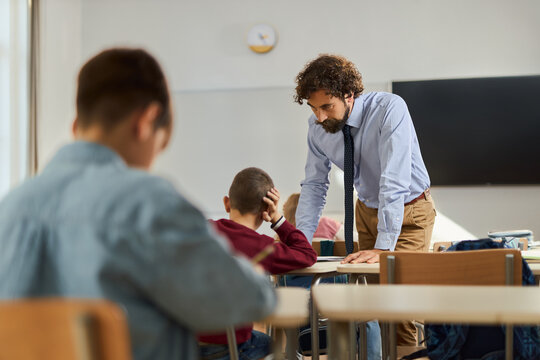 Young male professor assisting elementary schoolboy on a class at school.
