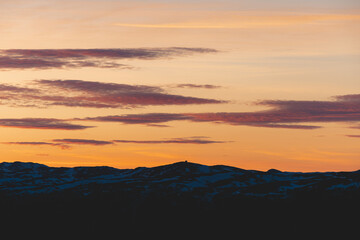 Evening light shines across Gaustatoppen Mountain near Rjukan, Norway. Snow patches and orange sky create a calm, majestic landscape of Nordic wilderness