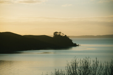 The sea reflecting the sunlight at sunset with distant hills in the background.