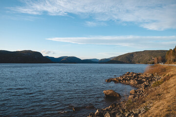 Golden light over calm lake in Setesdal Valley, Norway. Gentle hills and still water reflect warm sunset tones, capturing peaceful essence of Norwegian wilderness
