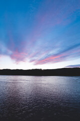 Soft pastel clouds reflect in calm lake water during sunset in Setesdal Valley, Norway. Peaceful Scandinavian evening atmosphere full of serenity and natural beauty