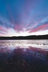 Soft pastel clouds reflect in calm lake water during sunset in Setesdal Valley, Norway. Peaceful Scandinavian evening atmosphere full of serenity and natural beauty
