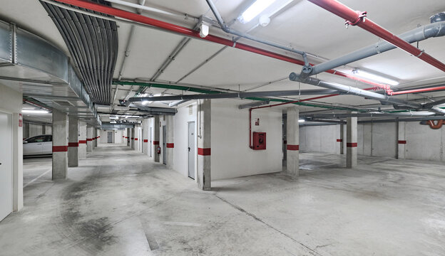 Clean and spacious underground parking garage with ventilation ducts, pipes, and red safety markings on concrete walls and columns