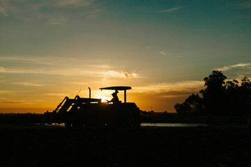 Farmer driving tractor in silhouette working agricultural field during vibrant golden sunset hour