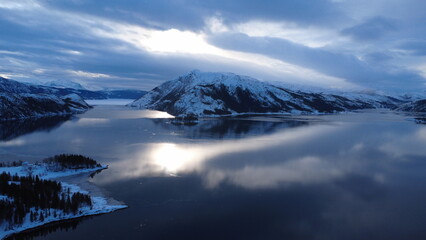 A stunning drone capture of a fjord at the base, surrounded by towering snowy mountains. The sky...
