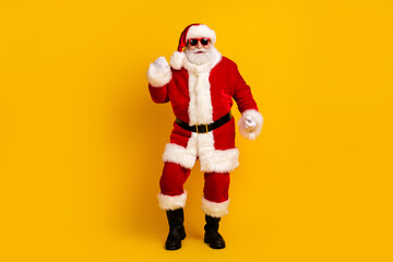 Santa Claus in red costume with white fur trim wears sunglass and strikes a fun pose against a bright yellow background for Christmas stock
