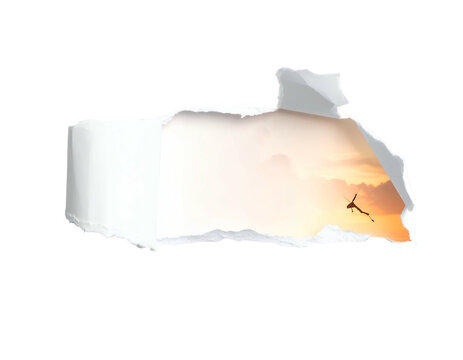 Torn paper reveals silhouette of person jumping against sunset