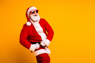 Santa in a red costume with white beard and hat poses cheerfully yellow background wearing shades and a black belt for a festive Christmas stock photo