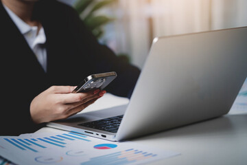 A woman is sitting at a desk with a laptop and a cell phone