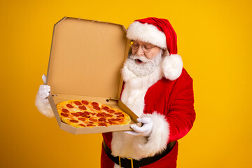 Santa holds a pizza in a box smiling man in red suit and hat against bright yellow background for...