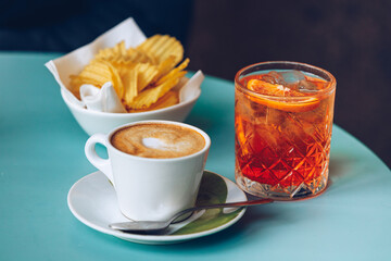 A cup of cappuccino, plate with potato chips and a glass with spritz-cocktail. 