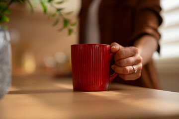 Woman holding red mug on wooden breakfast table
