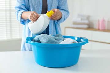 Woman with detergent near white table with plastic basin full of towels indoors, closeup
