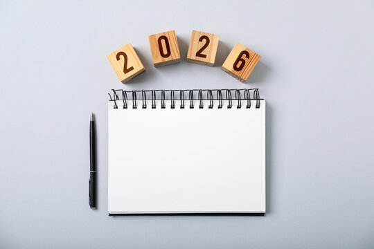 New 2026 year. Cubes with numbers, notebook and pen on grey background, top view