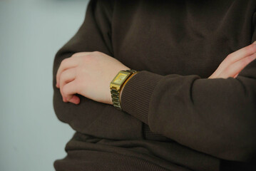 Fototapeta premium Close-up of a person wearing a stylish gold watch on their wrist, with arms crossed, showcasing modern fashion and elegance in a relaxed indoor setting