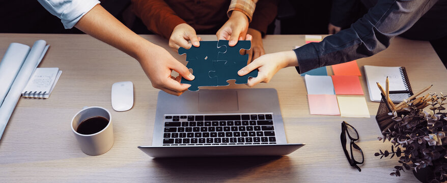 A diverse team actively collaborating during a brainstorming session, hands reaching for a puzzle piece, emphasizing teamwork, creativity, and problem-solving in a modern workspace. SACTR - Powered by Adobe