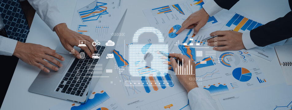 Business professionals collaborate over financial charts and data on a laptop, emphasizing digital security with a padlock icon in a modern office environment. Trope