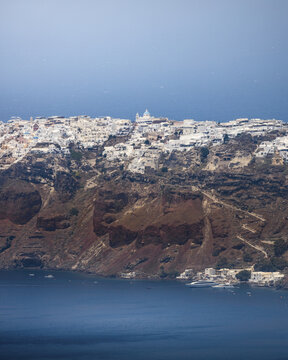 View of whitewashed buildings clinging to the dramatic cliffs above the azure sea, a mesmerising contrast of colors and textures, Fira, Thira, Greece.