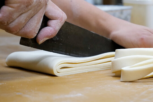 Close-up of a chef cutting folded dough sheets on a floured wooden surface, showing hand precision and smooth dough texture in a bakery kitchen.
