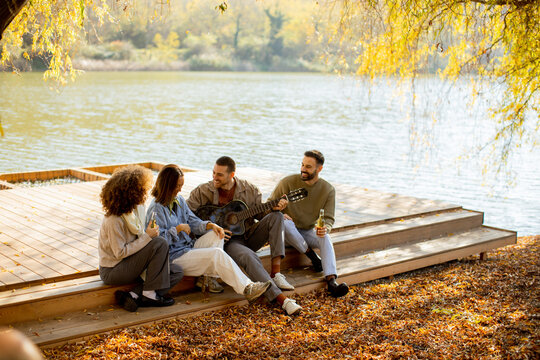 Friends gather by the lakeside enjoying music and laughter during a sunny autumn afternoon