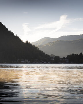 View of the serene lake mirroring the soft light and the dark silhouette of the mountains, creating a tranquil scene, Bled, Radovljica, Slovenia.