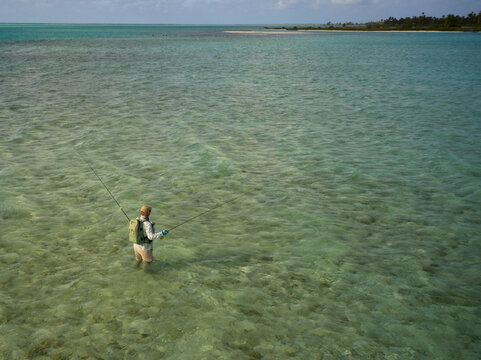 Aerial view of a lone fly fisherman wading across the crystal-clear flats of Kiritimati (Christmas Island), Kiribati, while casting for bonefish and giant trevally (GT). The pristine tropical lagoon, 