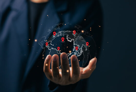 Businessman holding a digital globe with red location pins representing global network connection and worldwide business expansion powered by modern technology.