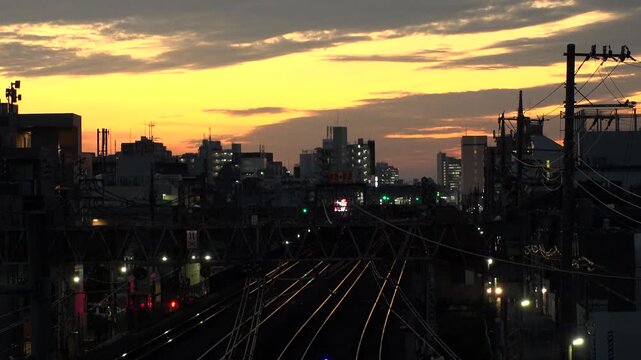 TOKYO, JAPAN - JUL 2025 : Sunset over a railway in a Tokyo residential area. A train arriving at the station during the golden hour, showcasing the daily commuter life. Time lapse shot, dusk to night.